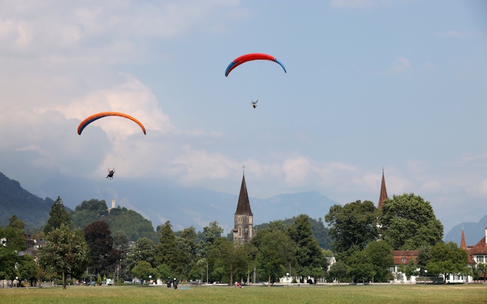 Paragliders soaring over Interlaken with church spires and mountains in the background.