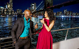 Couple toasting on a Premier Dinner Cruise with city skyline and bridge in the background.