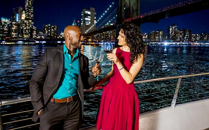 Couple toasting on a Premier Dinner Cruise with city skyline and bridge in the background.