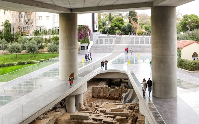 Visitors walking on a glass floor above ancient ruins at the Athens Acropolis Museum.