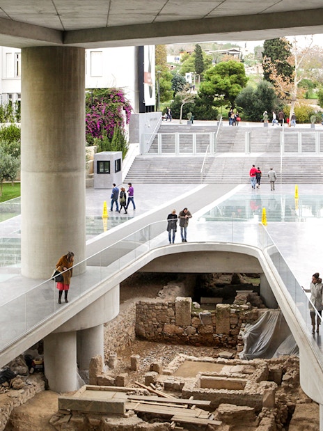 Visitors walking on a glass floor above ancient ruins at the Athens Acropolis Museum.