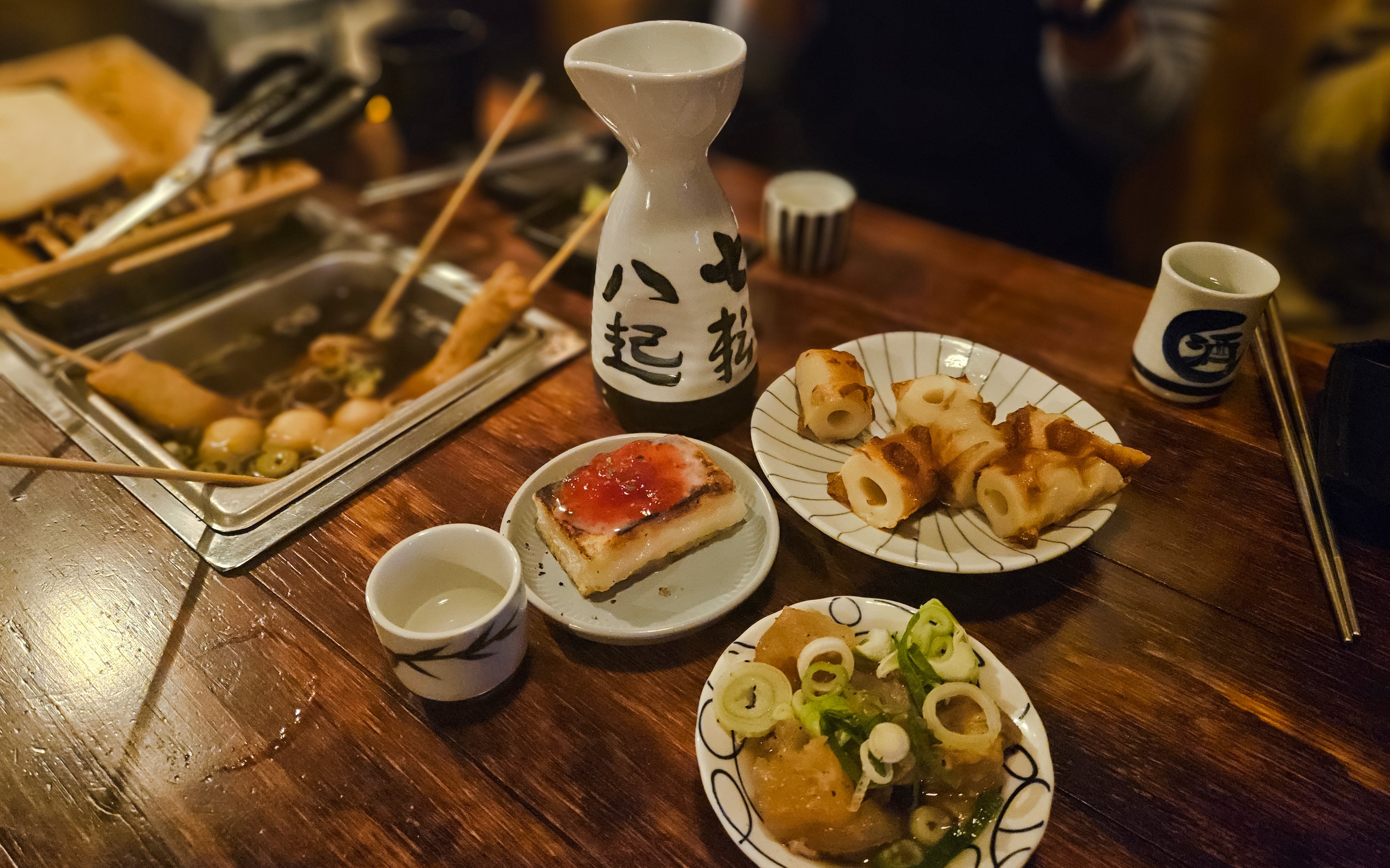 Japanese izakaya table with sake, grilled skewers, and traditional dishes.