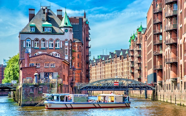 Harbor cruise boat passing historic brick buildings in Hamburg's Speicherstadt district.