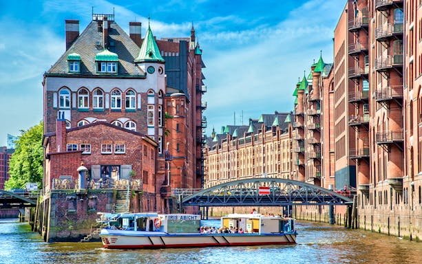 Harbor cruise boat passing historic brick buildings in Hamburg's Speicherstadt district.