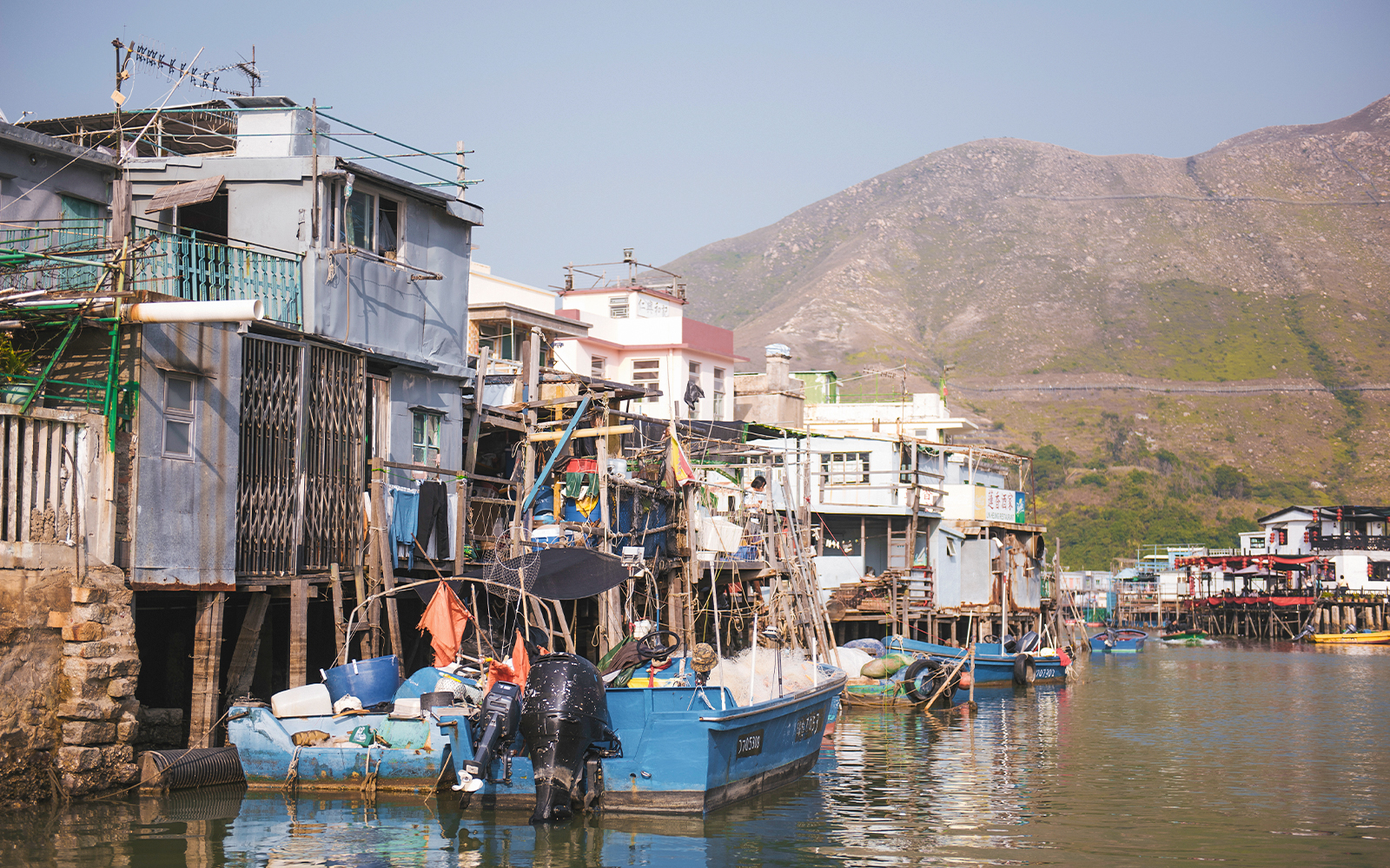 Stilt houses and fishing boats in Tai O village, Hong Kong, with mountains in the background.