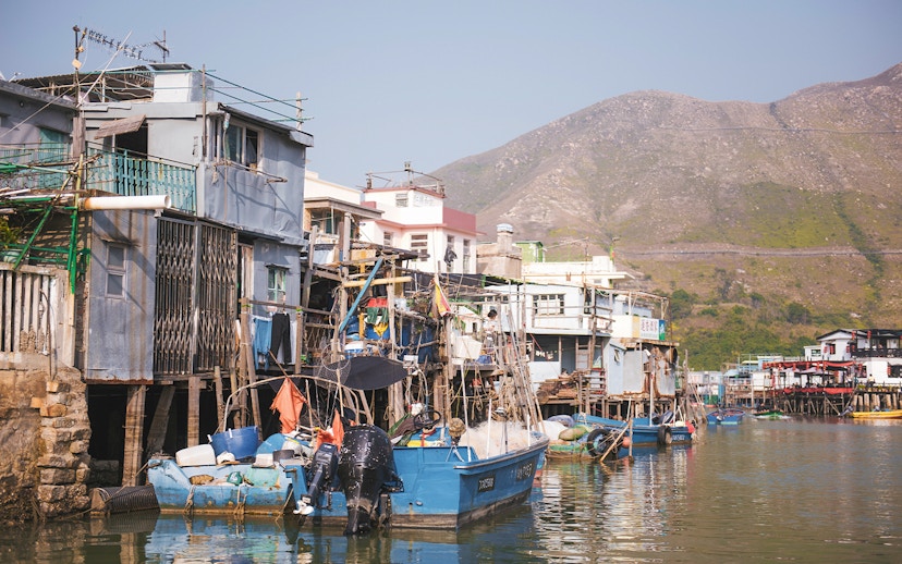 Stilt houses and fishing boats in Tai O village, Hong Kong, with mountains in the background.