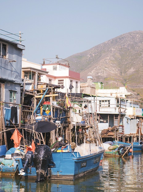 Stilt houses and fishing boats in Tai O village, Hong Kong, with mountains in the background.