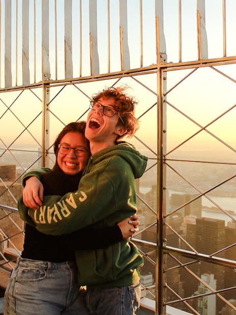 Guests embracing at Empire State Building observatory with New York City skyline at sunset.
