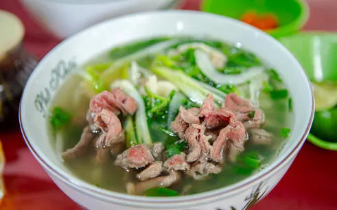 Bowl of Vietnamese pho with beef and herbs, part of Hanoi food tour.