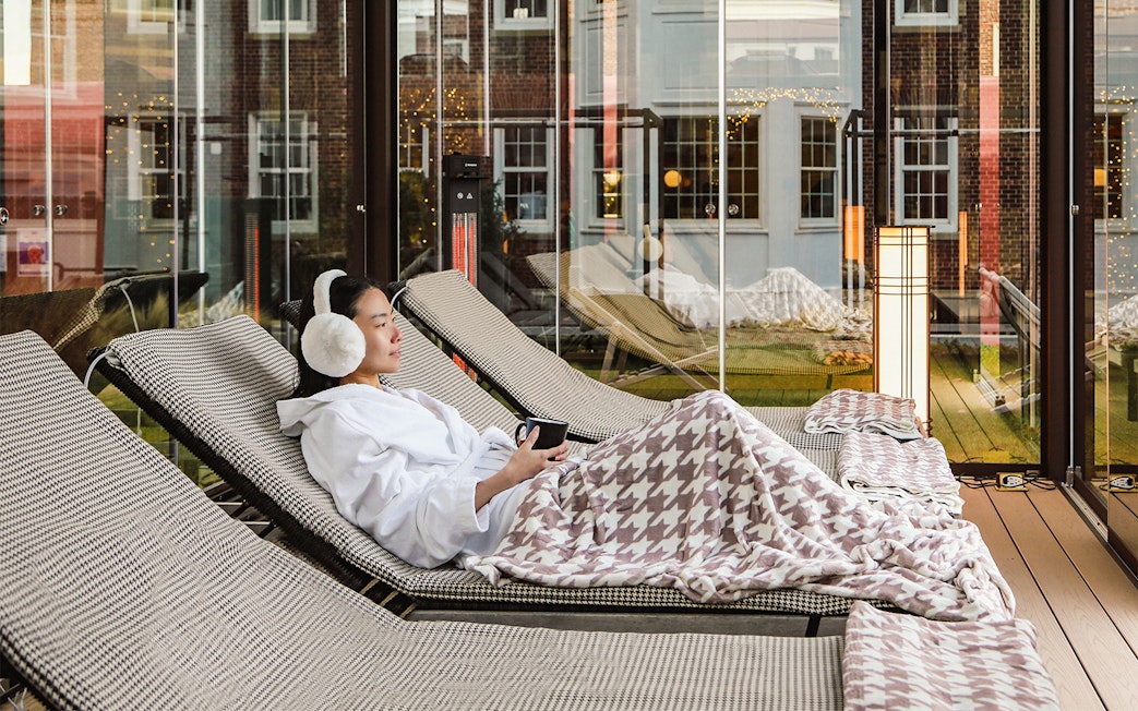 Person relaxing on a lounge chair with a blanket at QC New York spa.