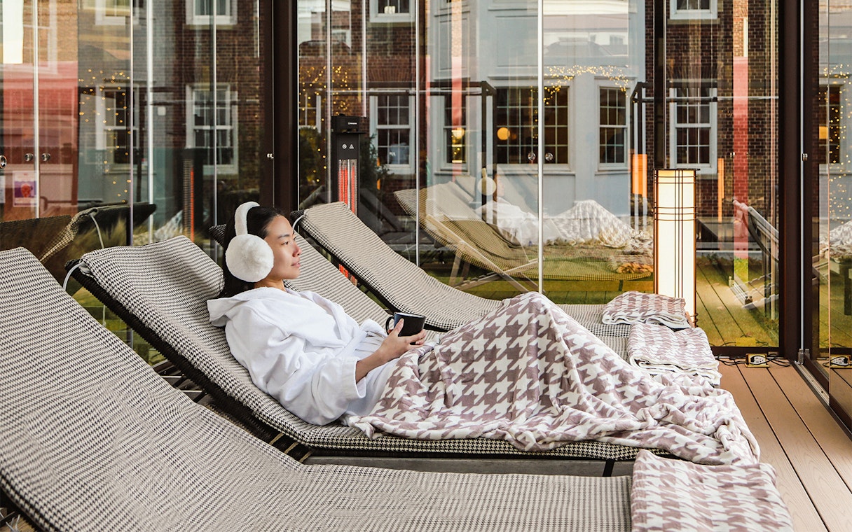 Person relaxing on a lounge chair with a blanket at QC New York spa.