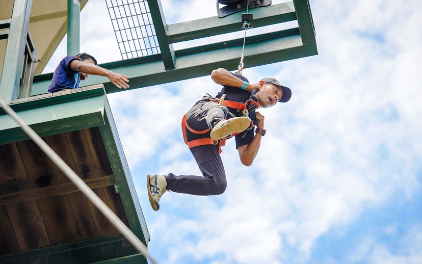 Person ziplining at Mega Adventure Park, Singapore against a blue sky.