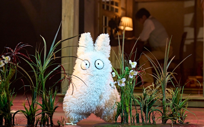 Furry creature on stage at My Neighbour Totoro West End show, surrounded by plants.