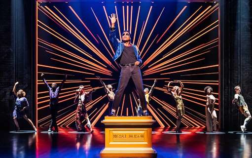 Performer on stage with dancers in MJ The Musical.