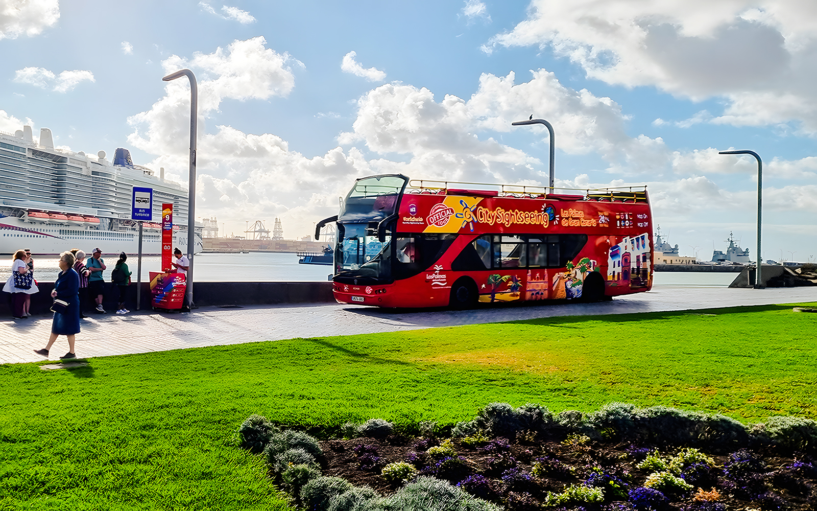 Red double-decker hop-on hop-off bus at Las Palmas de Gran Canaria port with cruise ship in background.
