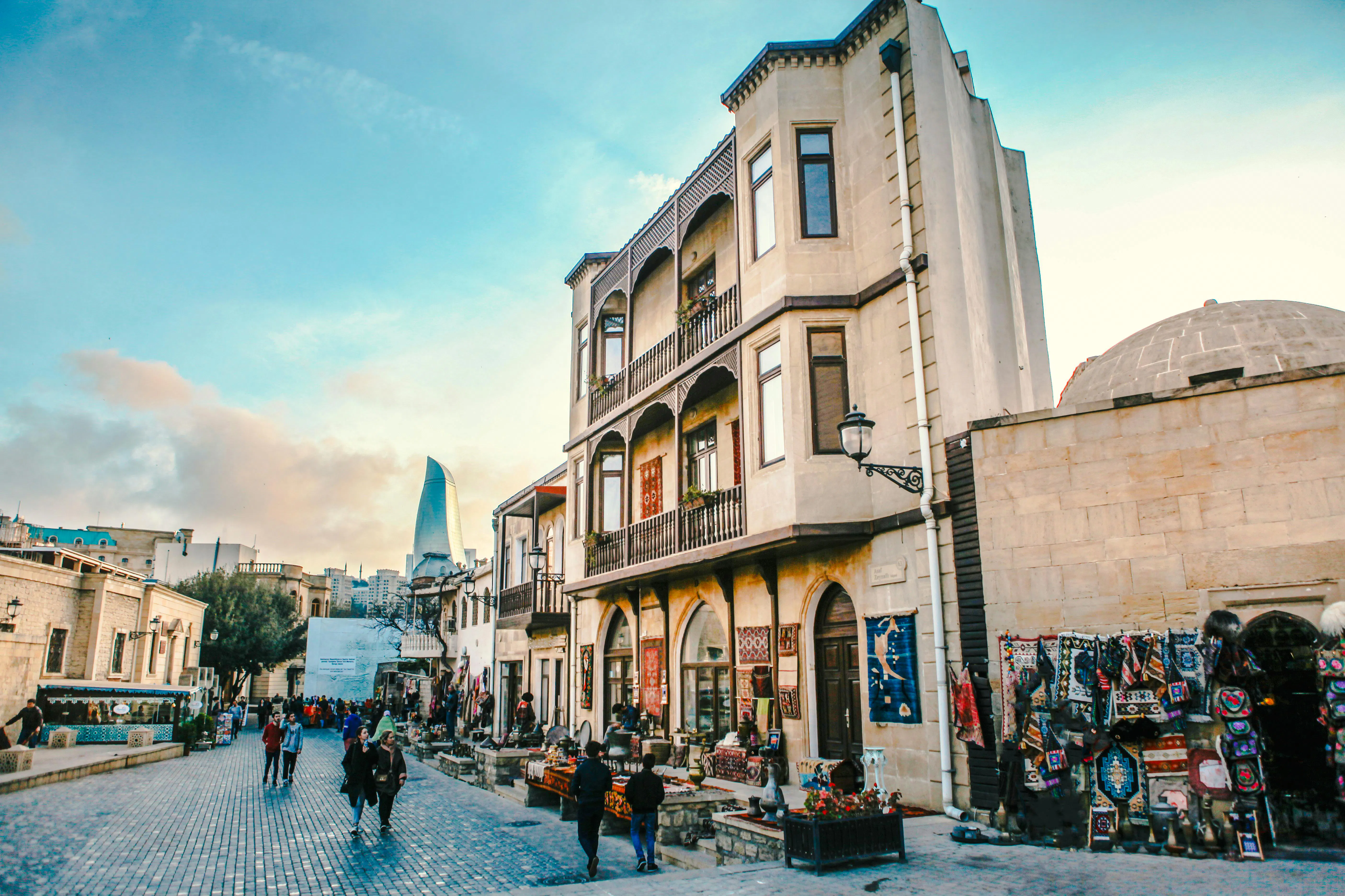 Old city street in Baku with traditional buildings and modern Flame Towers in the background.