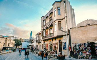 Old city street in Baku with traditional buildings and modern Flame Towers in the background.