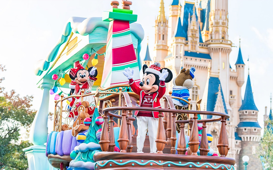 Mickey and Minnie Mouse on a festive parade float at Tokyo Disneyland with Cinderella Castle in the background.