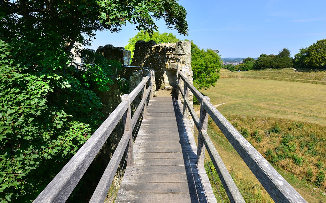 Walkway leading to Carisbrooke Castle ruins surrounded by greenery.