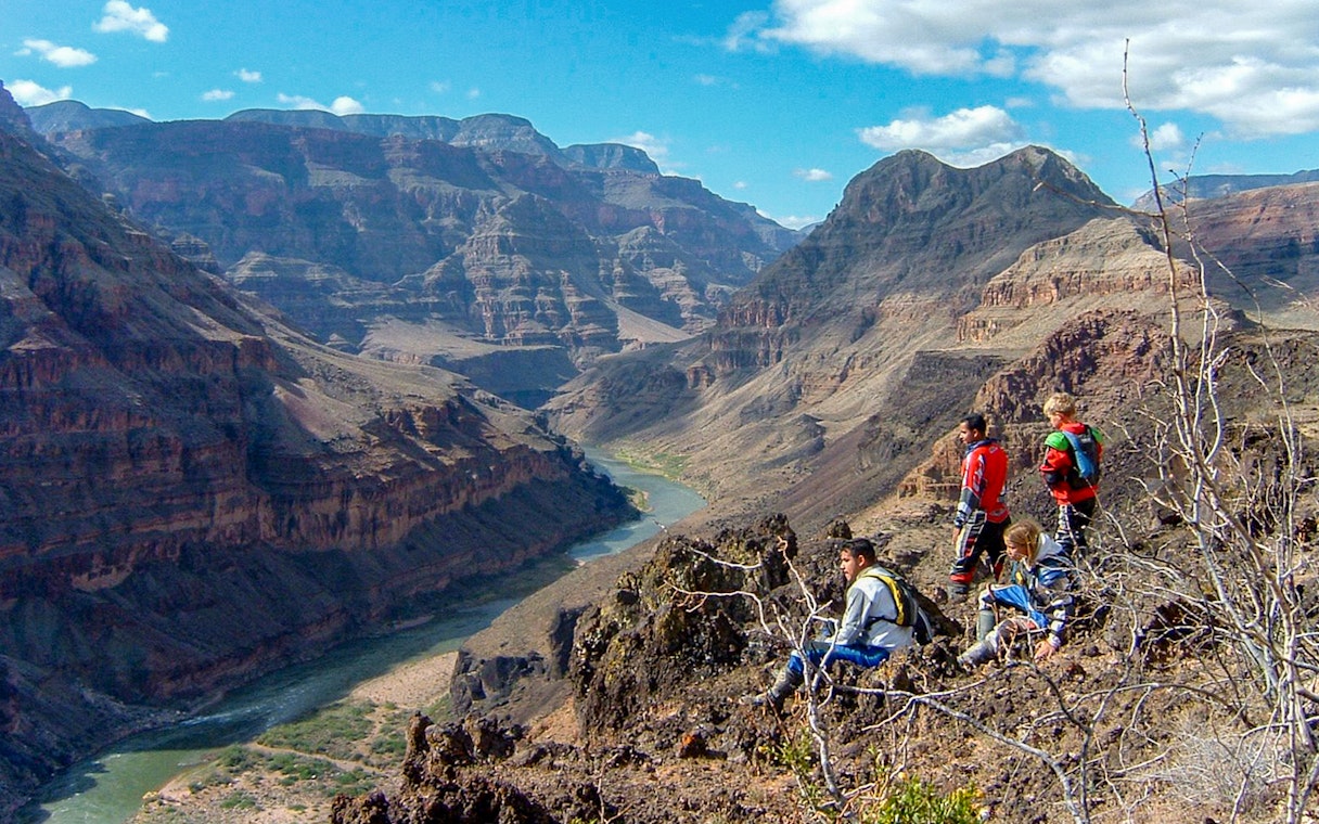 Tourists sitting and standing on a rocky ledge overlooking the Grand Canyon.