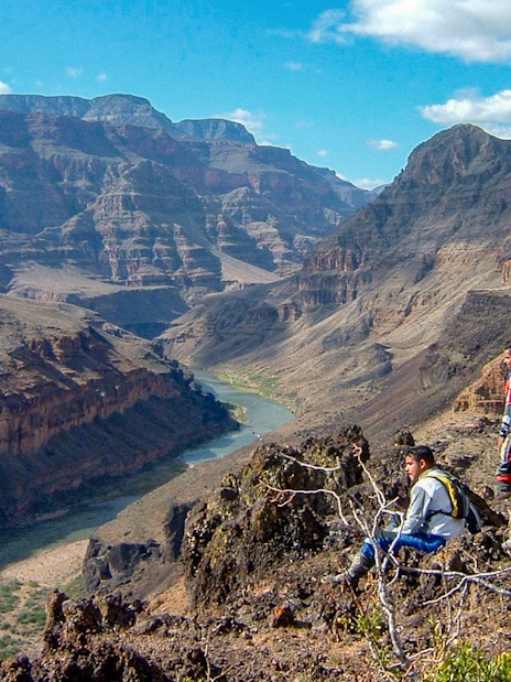 Tourists sitting and standing on a rocky ledge overlooking the Grand Canyon.