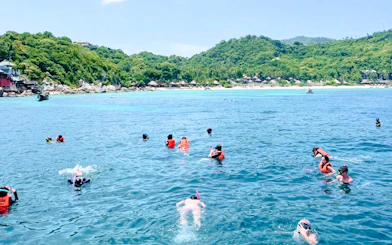 Snorkelers in the clear waters of Ang Thong Marine Park, Koh Samui, with lush islands in the background.