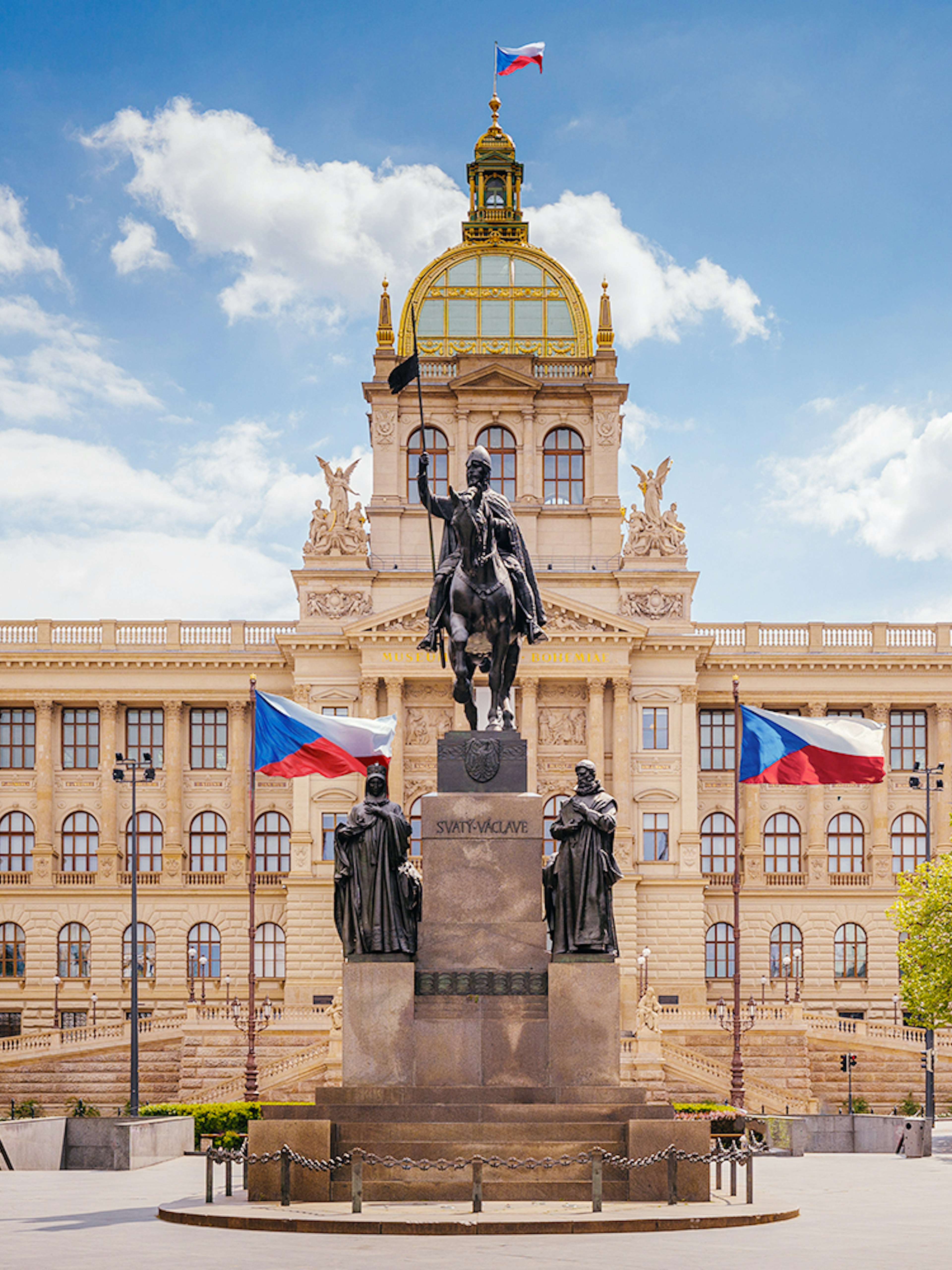 Prague National Museum with equestrian statue and Czech flags in front.