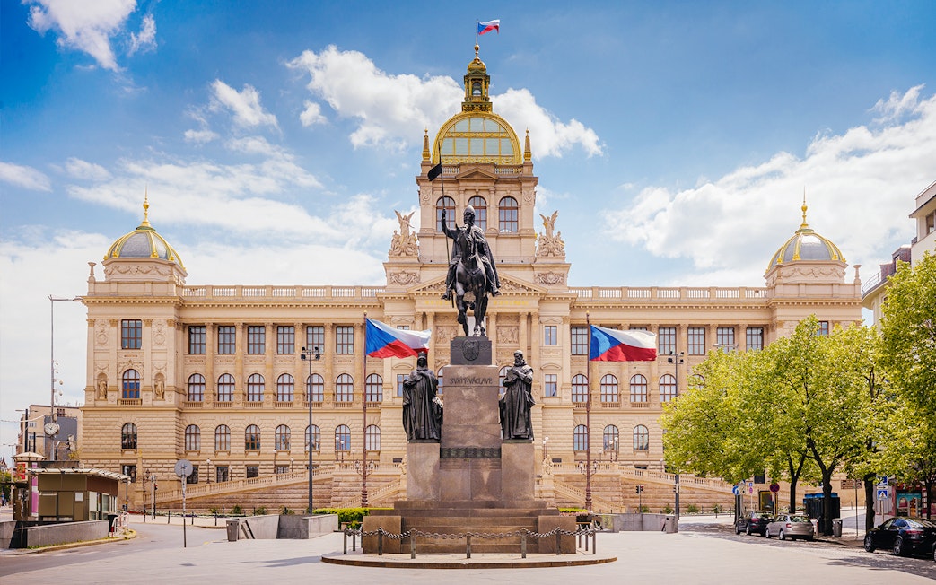 Prague National Museum with equestrian statue and Czech flags in front.