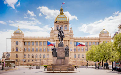 Prague National Museum with equestrian statue and Czech flags in front.