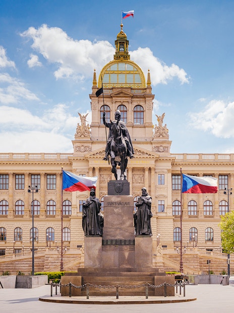 Prague National Museum with equestrian statue and Czech flags in front.