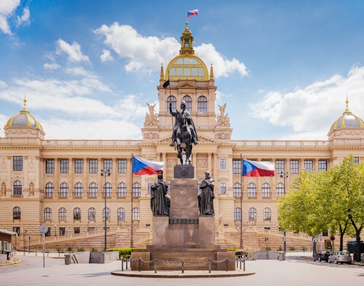 Prague National Museum with equestrian statue and Czech flags in front.