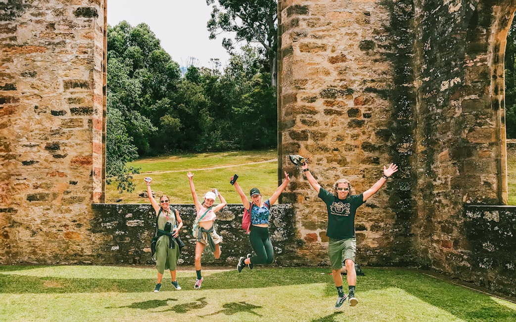 Visitors jumping joyfully at Port Arthur historic site during a full-day guided tour.
