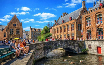Bruges canal with historic buildings and tourists on a bridge during a full-day tour from Amsterdam.