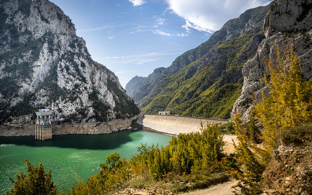 Bovilla Lake dam reservoir surrounded by rocky mountains and green foliage.