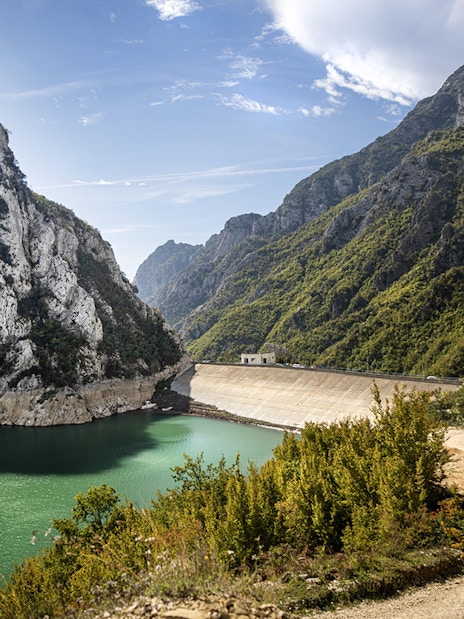 Bovilla Lake dam reservoir surrounded by rocky mountains and green foliage.