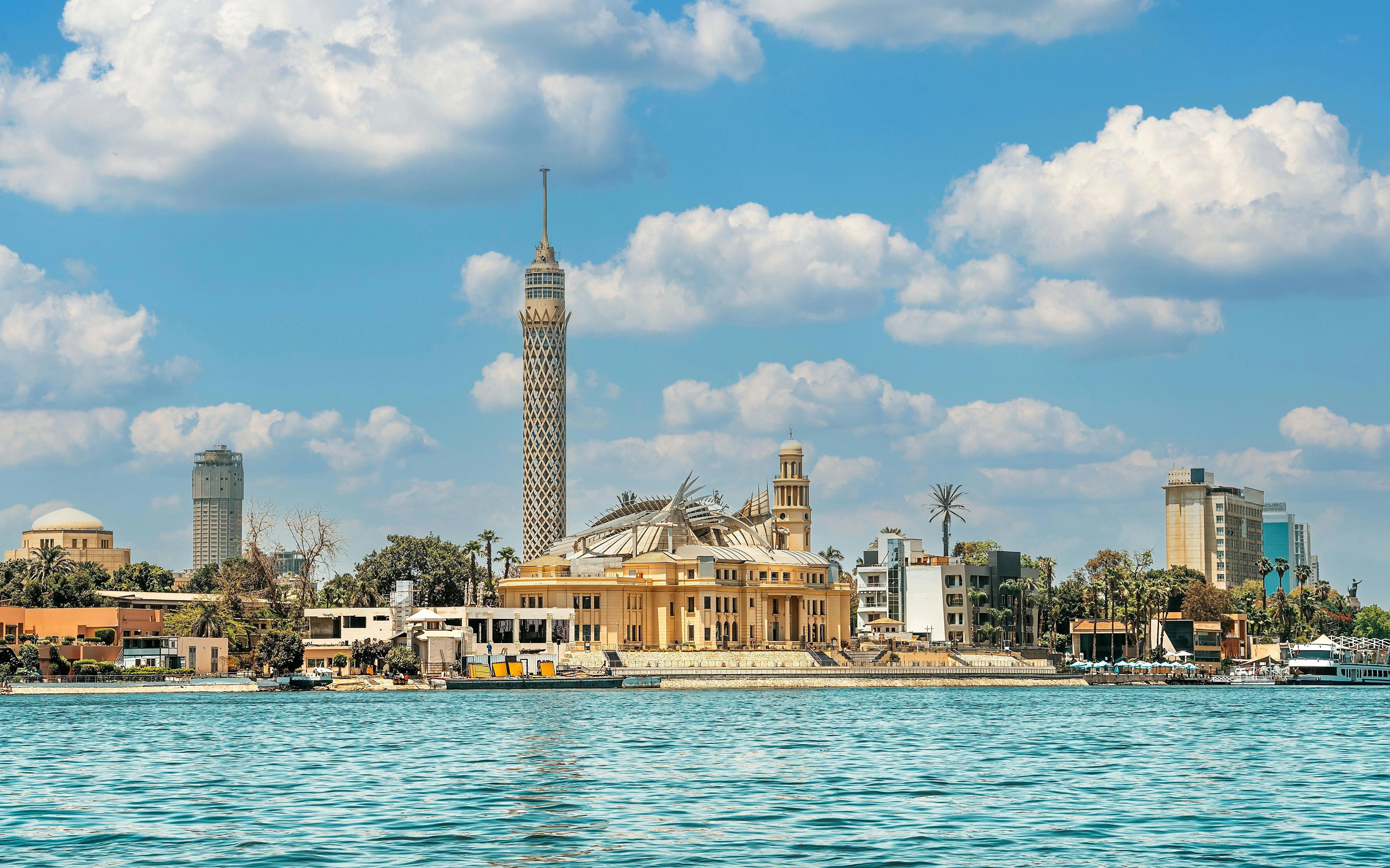 Cairo Tower with Nile River in foreground, surrounded by cityscape.