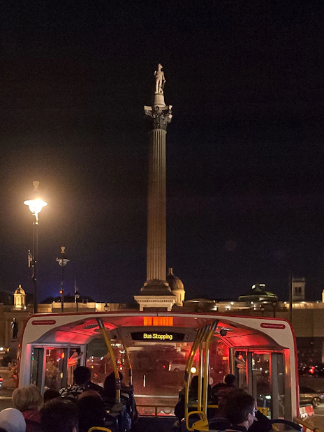 Open-top bus tour at night near Nelson's Column, London.