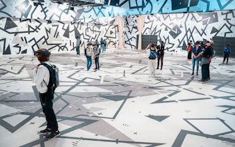 Visitors wearing VR headsets in a geometric-patterned room for the Eternal Notre-Dame VR Experience.