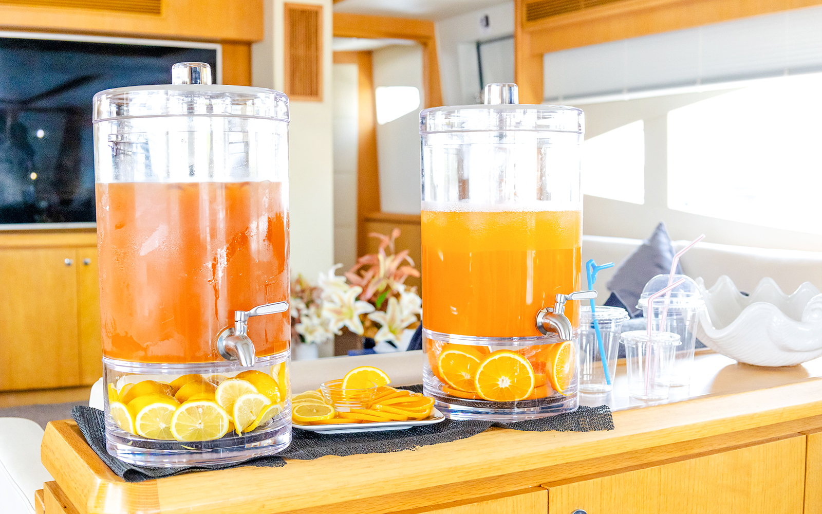 Orange juice dispensers on yacht interior with sliced citrus fruits.