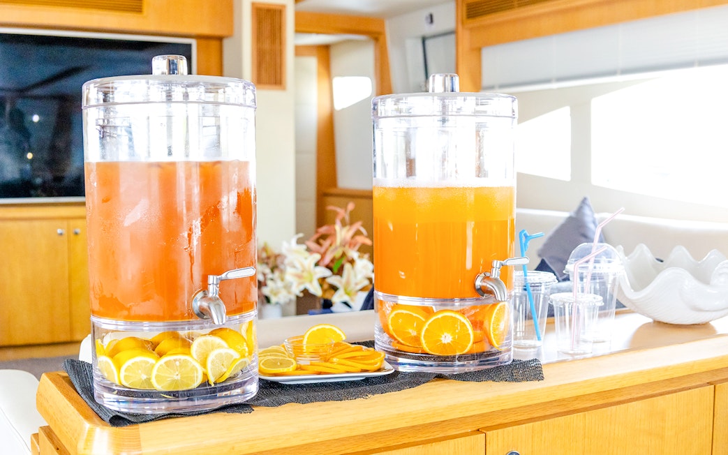 Orange juice dispensers on yacht interior with sliced citrus fruits.