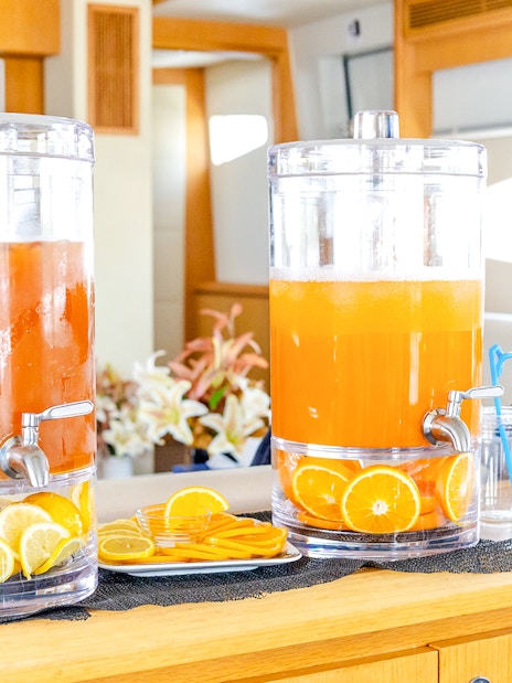 Orange juice dispensers on yacht interior with sliced citrus fruits.