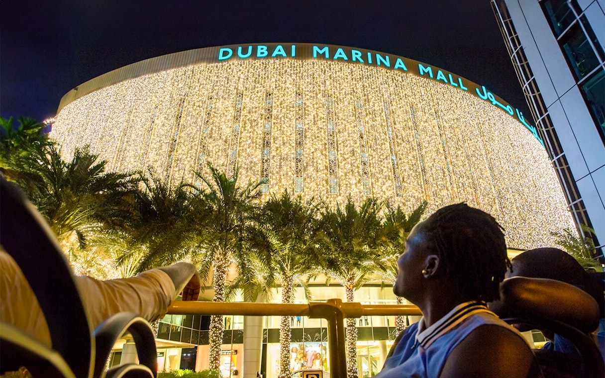 Visitors admire Dubai Marina Mall illuminated at night.
