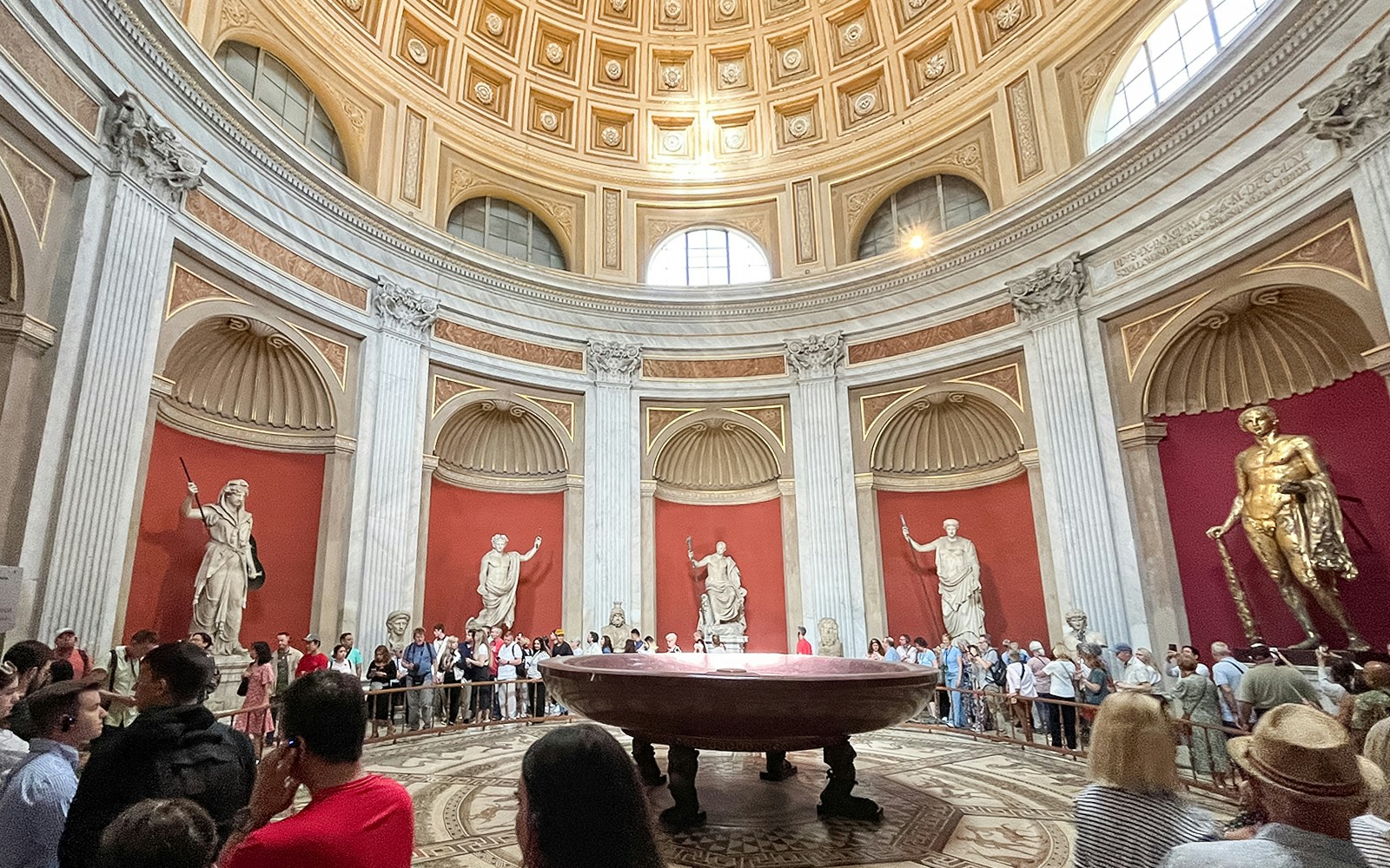 Visitors in Sala Rotonda, Vatican Museums, surrounded by classical statues and ornate architecture.