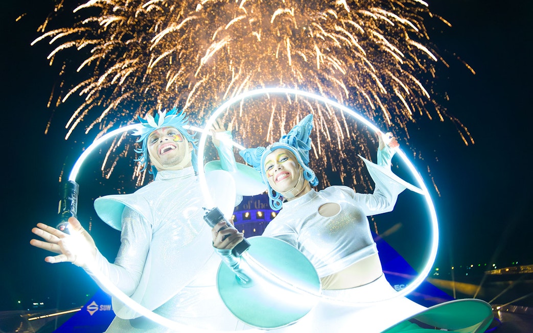 Performers with glowing hoops at Kiss of the Sea Show, fireworks in the background.