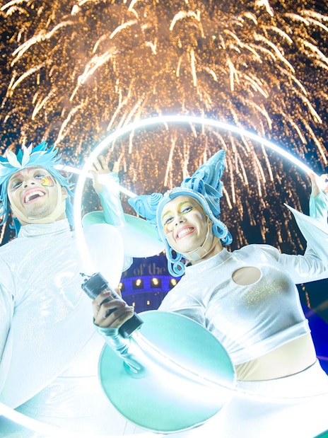 Performers with glowing hoops at Kiss of the Sea Show, fireworks in the background.