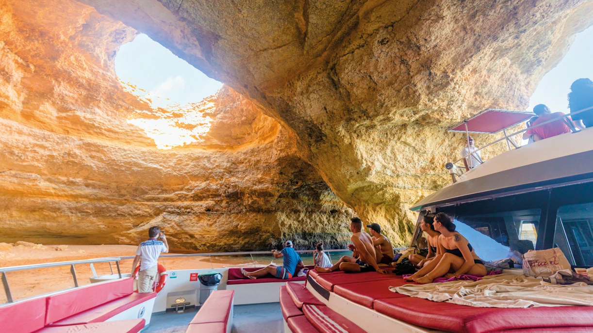 Boat tour inside Benagil Caves, Algarve, Portugal, with tourists observing rock formations.
