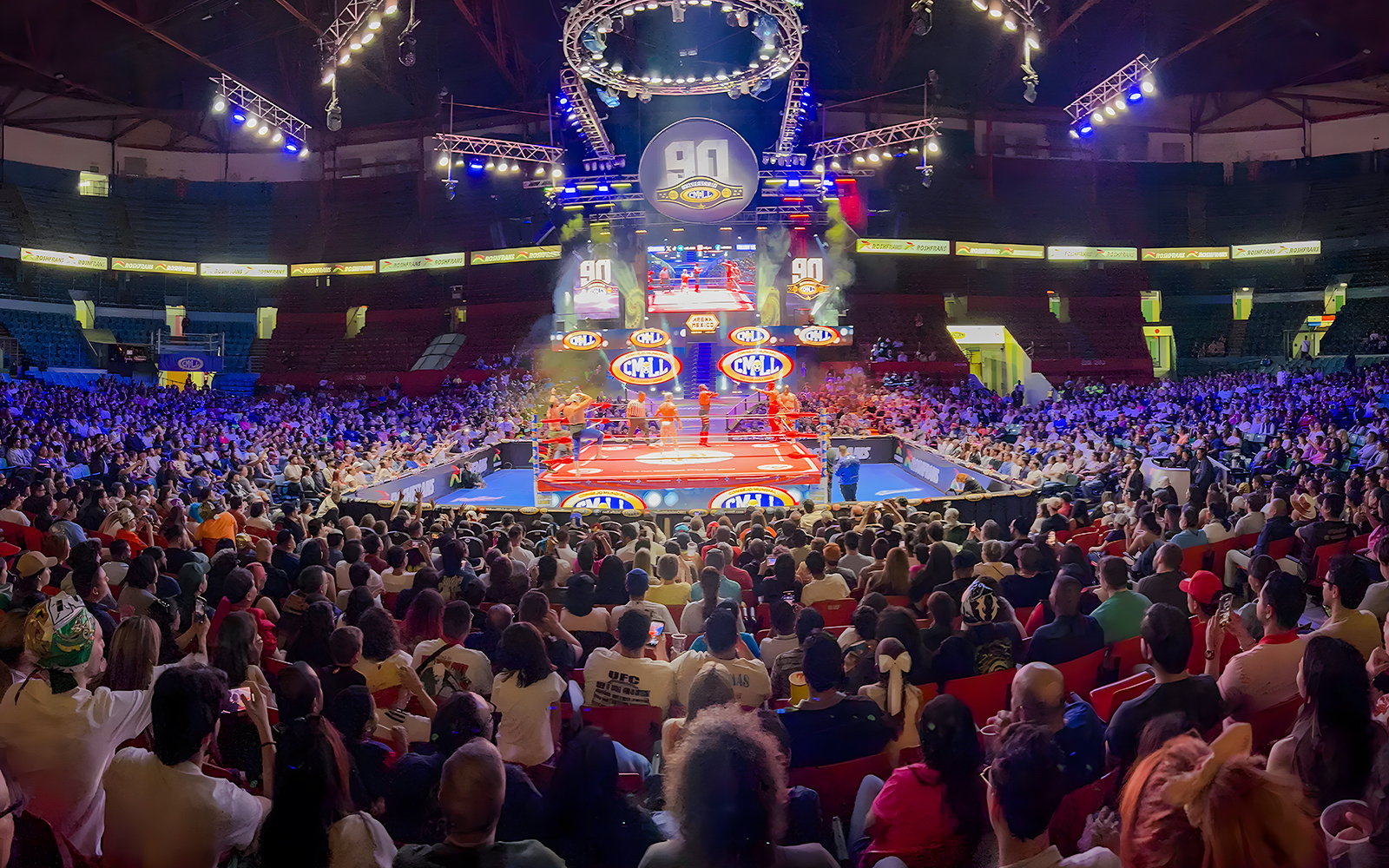 Crowd watching a lively lucha libre wrestling match in a packed arena.