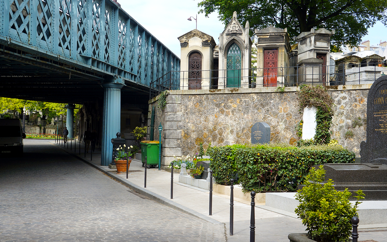 Montmartre Cemetery under bridge in Paris, featuring ornate tombs and greenery.