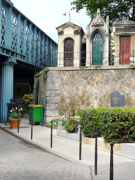 Montmartre Cemetery under bridge in Paris, featuring ornate tombs and greenery.