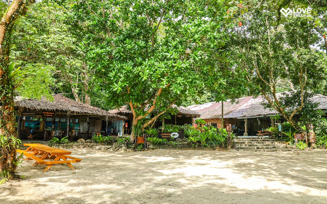 Thatched-roof buildings and picnic tables on a sandy clearing in the Surin Islands.